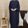 Beautiful woman wearing navy blue abaya and beige hijab, standing indoors with cozy decor.