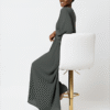 Stylish woman in modest, flowy gray dress with headwrap, sitting on a white stool for fashion and modestwear.
