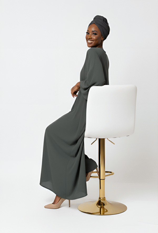 Stylish woman in modest, flowy gray dress with headwrap, sitting on a white stool for fashion and modestwear.