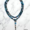 Blue gemstone beaded necklace with silver pendant on marble background.