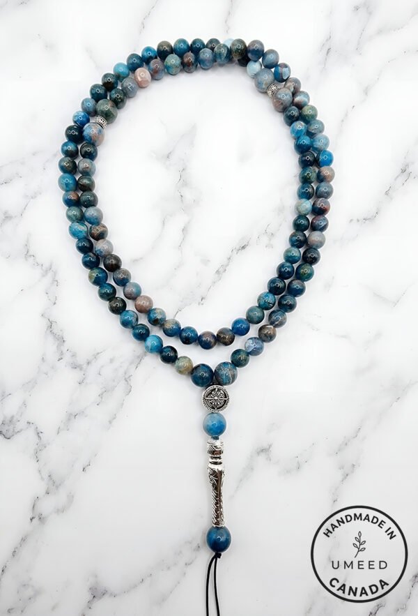 Blue gemstone beaded necklace with silver pendant on marble background.
