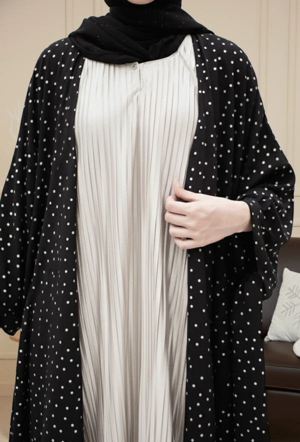 Close-up of modest fashion dress featuring pleated white fabric with a black polka dot outer layer, stylish and comfortable for women.