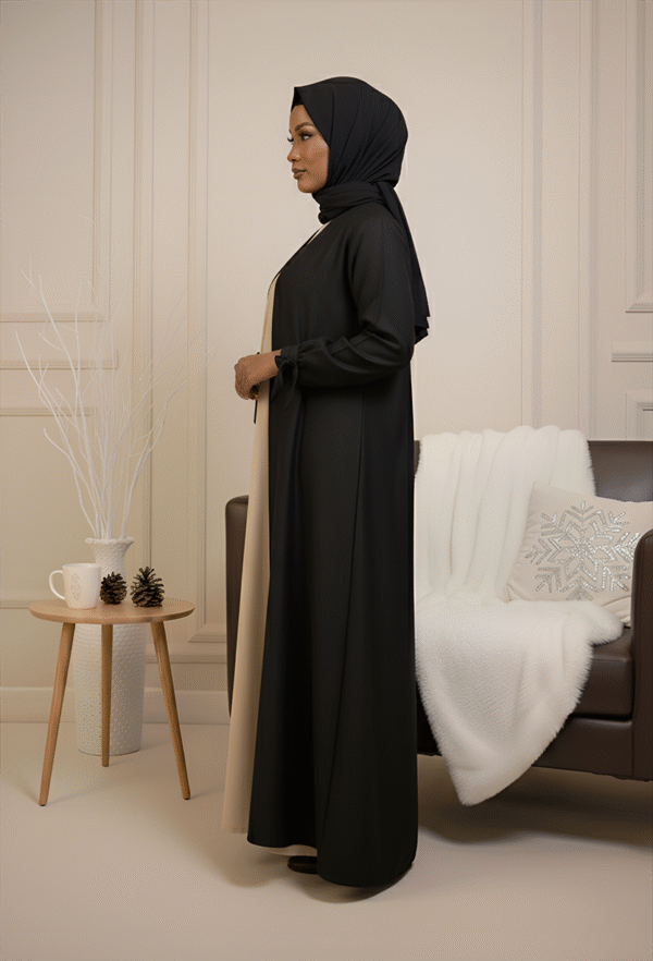 Stylish woman wearing black and beige abaya with hijab, elegant decor for modest fashion showcase.