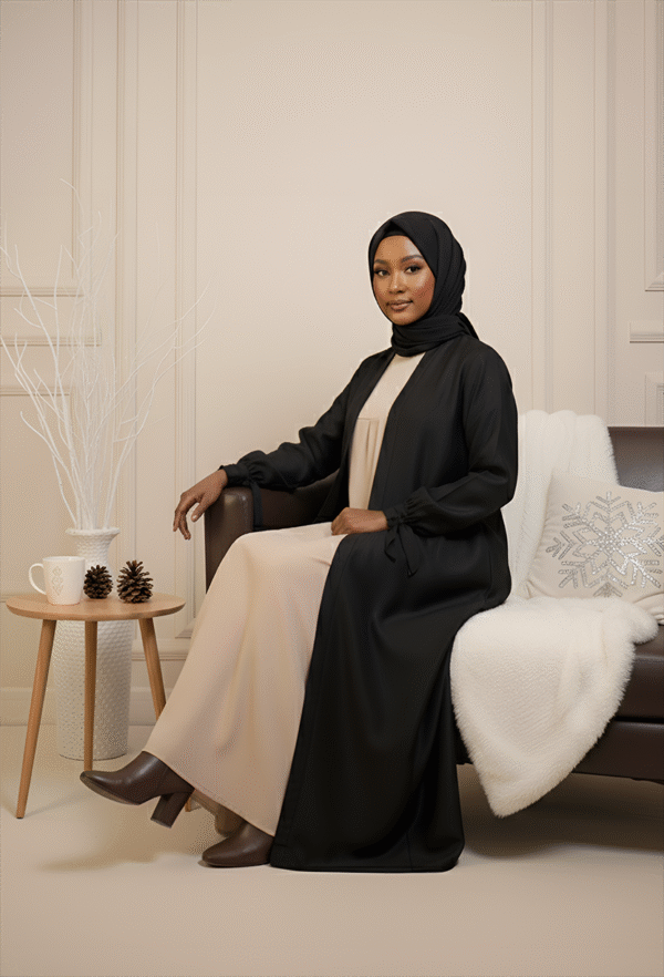 Beautiful woman wearing stylish modest black and beige outfit with hijab, cozy winter decor.