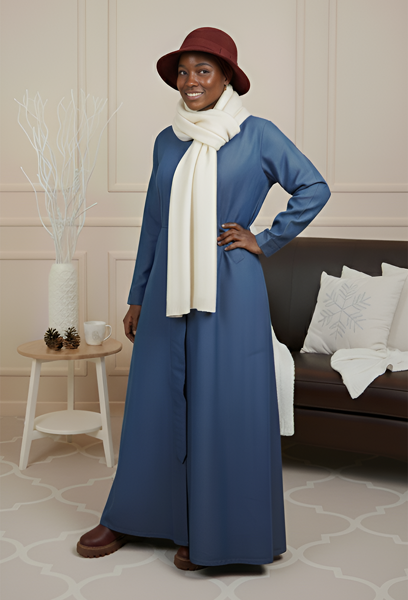 Chic women’s fashion featuring a long blue dress, warm scarf, stylish hat, and brown boots. Perfect for seasonal styling.