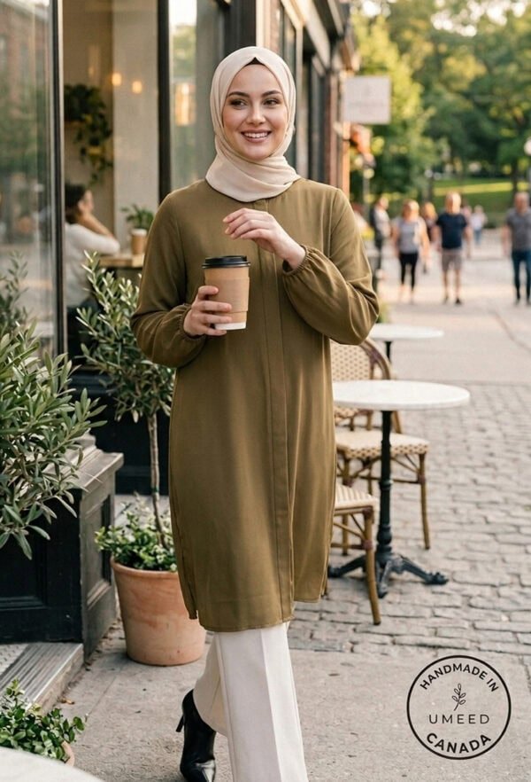 A smiling woman in a beige hijab and olive green dress holding coffee outside a café in a lively cit.