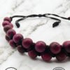 Handmade purple beaded necklace with black cord on marble surface.