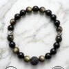 Black and gold beaded bracelet with a lava stone centerpiece on a white marble background.
