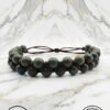 Handmade beaded bracelet with green beads and leather cord on marble background.