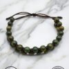Handmade green beaded bracelet with adjustable cord on marble surface.