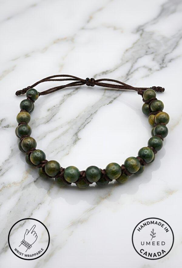 Handmade green beaded bracelet with adjustable cord on marble surface.