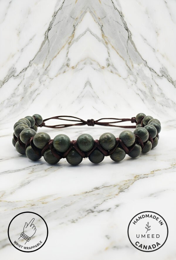 Handmade beaded bracelet with green beads and leather cord on marble background.