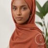 Elegant woman wearing a rust-colored hijab with a neutral background.