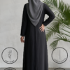Elegant woman in black abaya with hijab standing near a green plant.